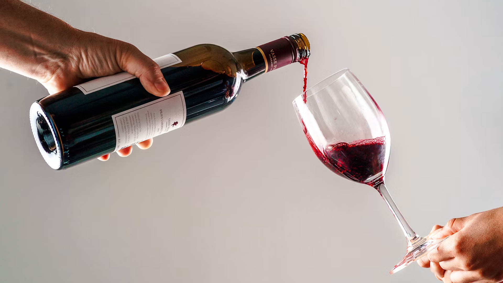 Botella de vino tinto con la etiqueta a la vista mientras se sirve en una copa